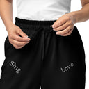 Front close-up view of female model in black unisex wide-leg joggers with tonal words ‘Sing, Dance, Pray, Laugh, Love, LIVE’ scattered across legs