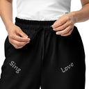 Front close-up view of female model in black unisex wide-leg joggers with tonal words ‘Sing, Dance, Pray, Laugh, Love, LIVE’ scattered across legs
