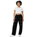 Front view of female model in black unisex wide-leg pants with tonal words ‘Sing, Dance, Pray, Laugh, Love, LIVE’ scattered across legs