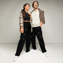Front view of  male and female models in black unisex wide-leg joggers with tonal words ‘Sing, Dance, Pray, Laugh, Love, LIVE’ scattered across legs