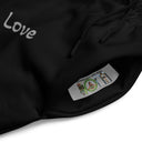 Close-up pocket view of black unisex wide-leg joggers with tonal words ‘Sing, Dance, Pray, Laugh, Love, LIVE’ scattered across legs