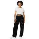 Front view of female model in black unisex wide-leg pants with tonal words ‘Sing, Dance, Pray, Laugh, Love, LIVE’ scattered across legs